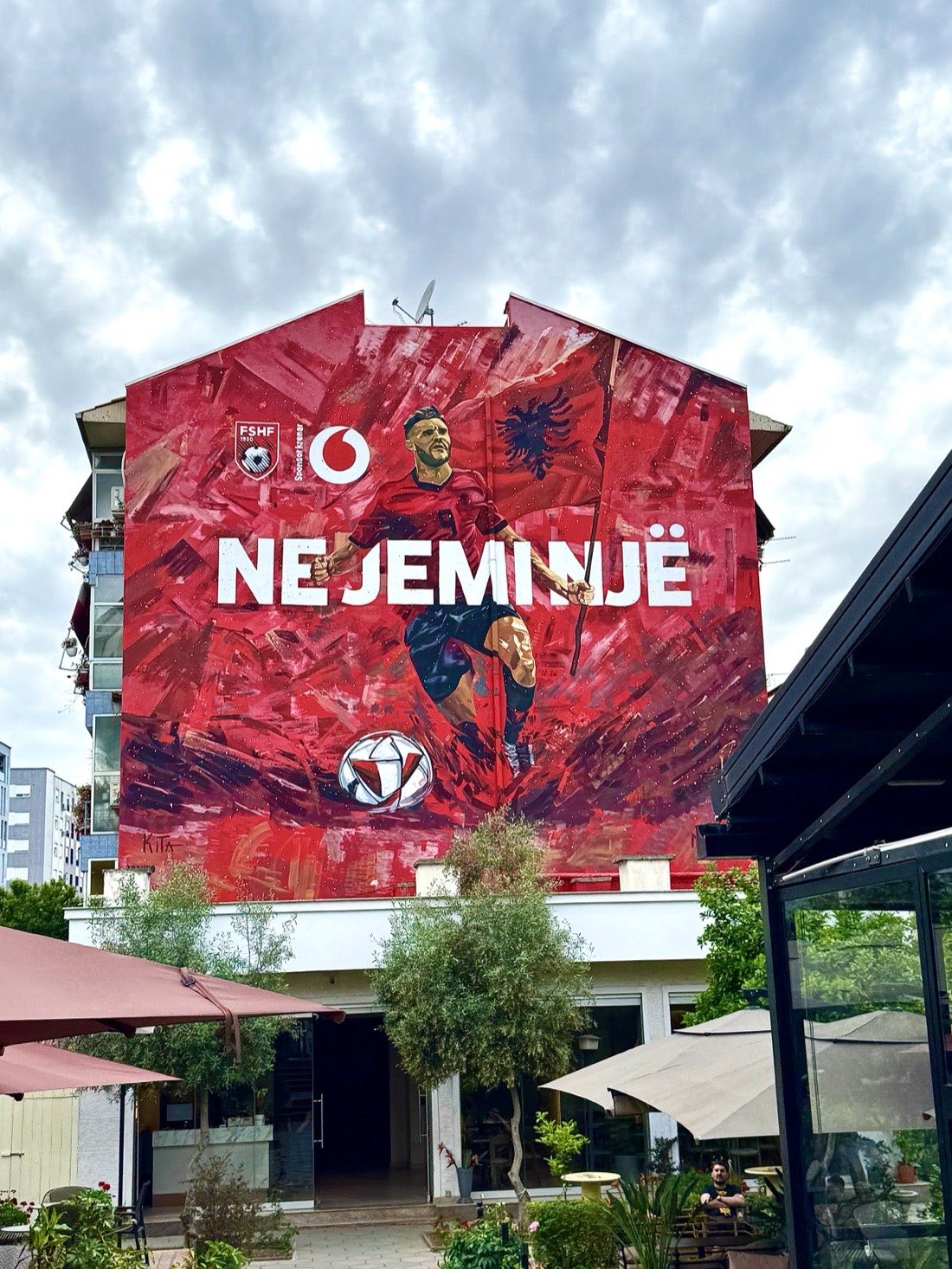 A Tirana mural in red and black showing an Albanian footballer and the words NE JEMI NJË — We Are One
