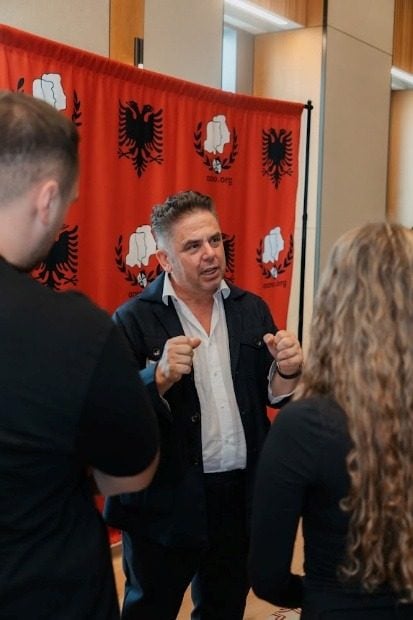 Një pjesëmarrës duke folur me dy studentë pranë sfondit të AANO-s.