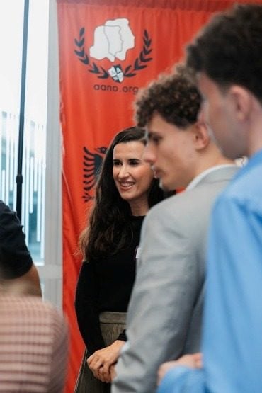 Studentë dhe profesionistë duke biseduar pranë sfondit të AANO-s.