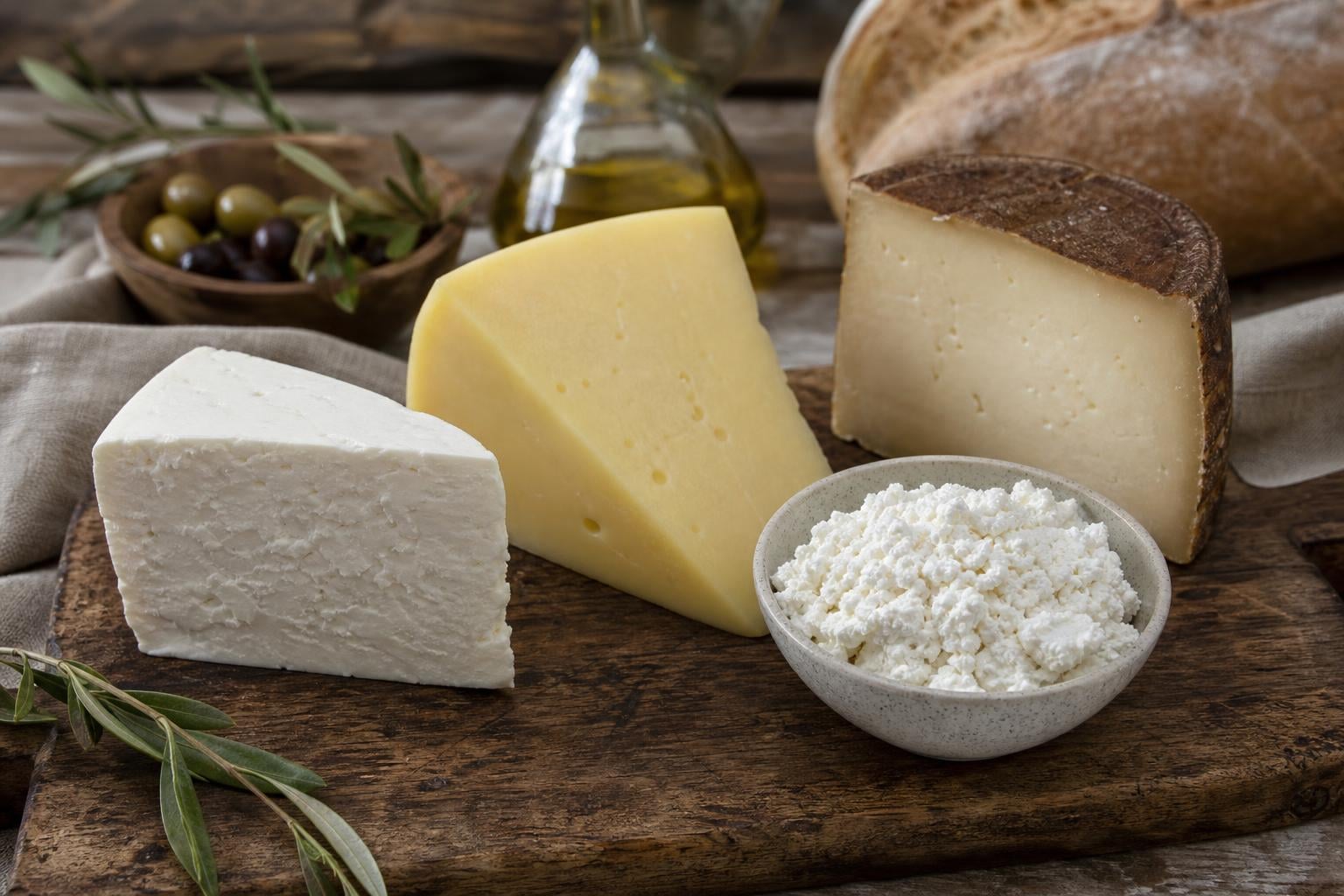 Four wedges of Albanian cheese on a wooden board: white brined djathë i bardhë, yellow aged kaçkavall, fresh gjizë in a small bowl, and a darker rind sharri.