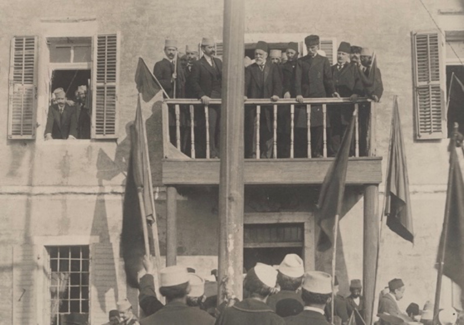 Ismail Qemali and his cabinet in Vlorë on 28 November 1913, marking the first anniversary of independence — the Skanderbeg flag visible behind them.