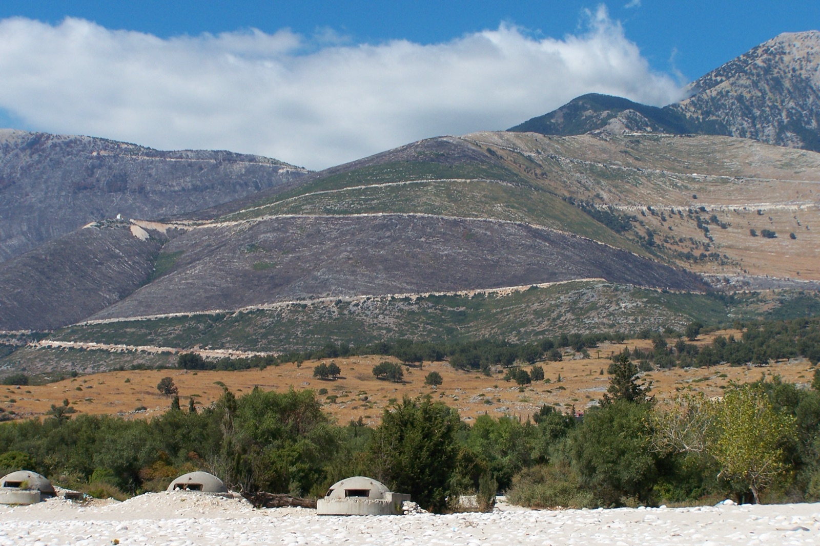 A line of concrete Hoxha-era bunkers along the beach at Dhërmi on the Albanian Riviera — survivors of a program that built six-figure numbers of pillboxes between 1967 and the early 1980s.