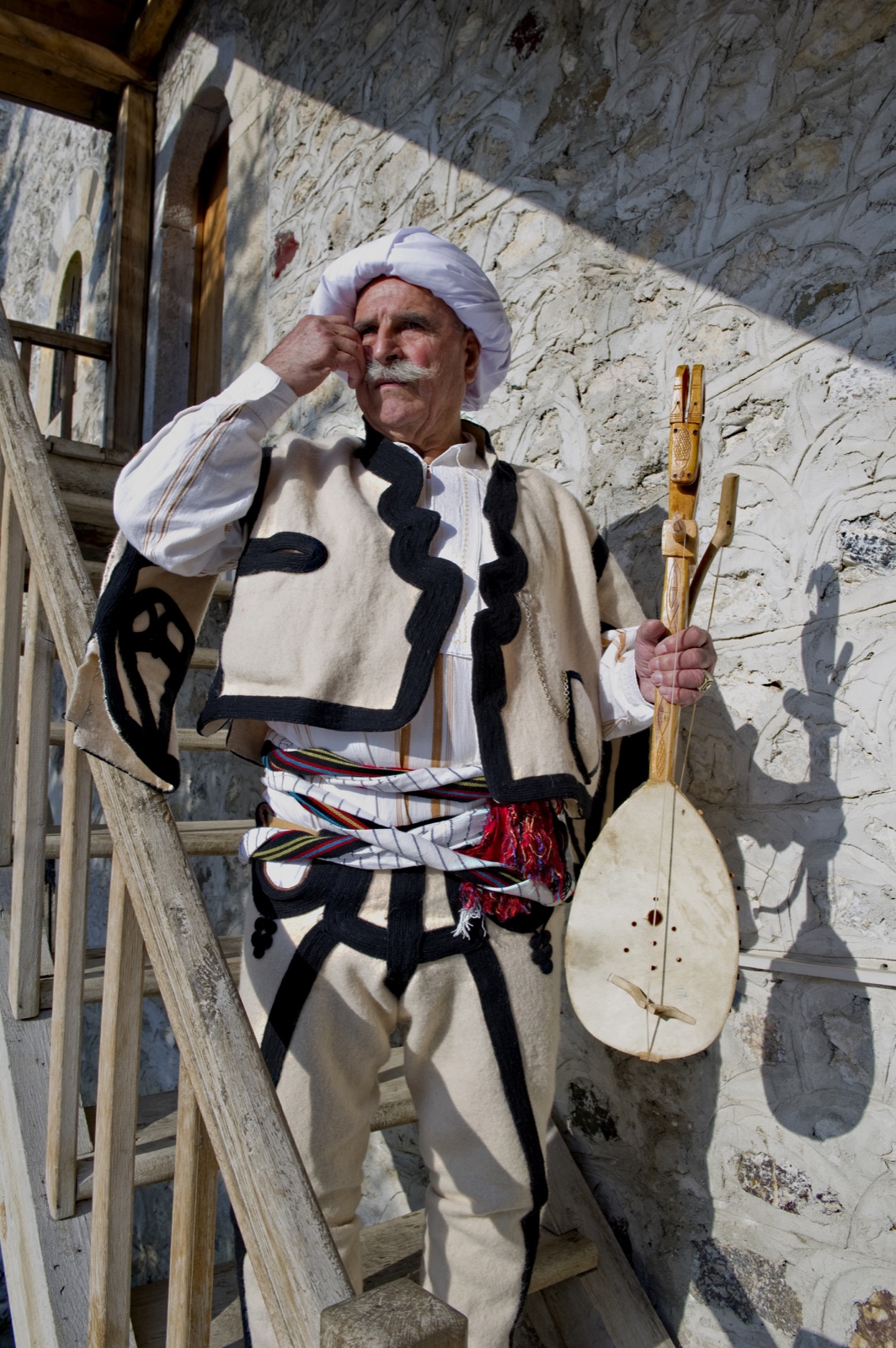 A lahutar in northern Albanian highland dress — qeleshe cap, white tunic, and lahutë drawn across the knee.
