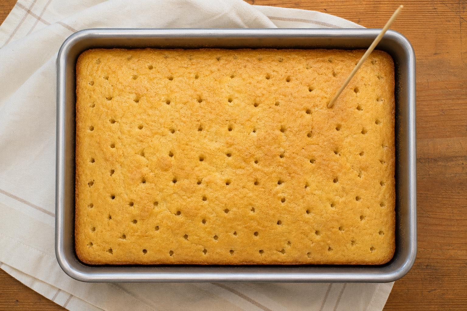 Poking holes across the baked sponge cake before the milk soak